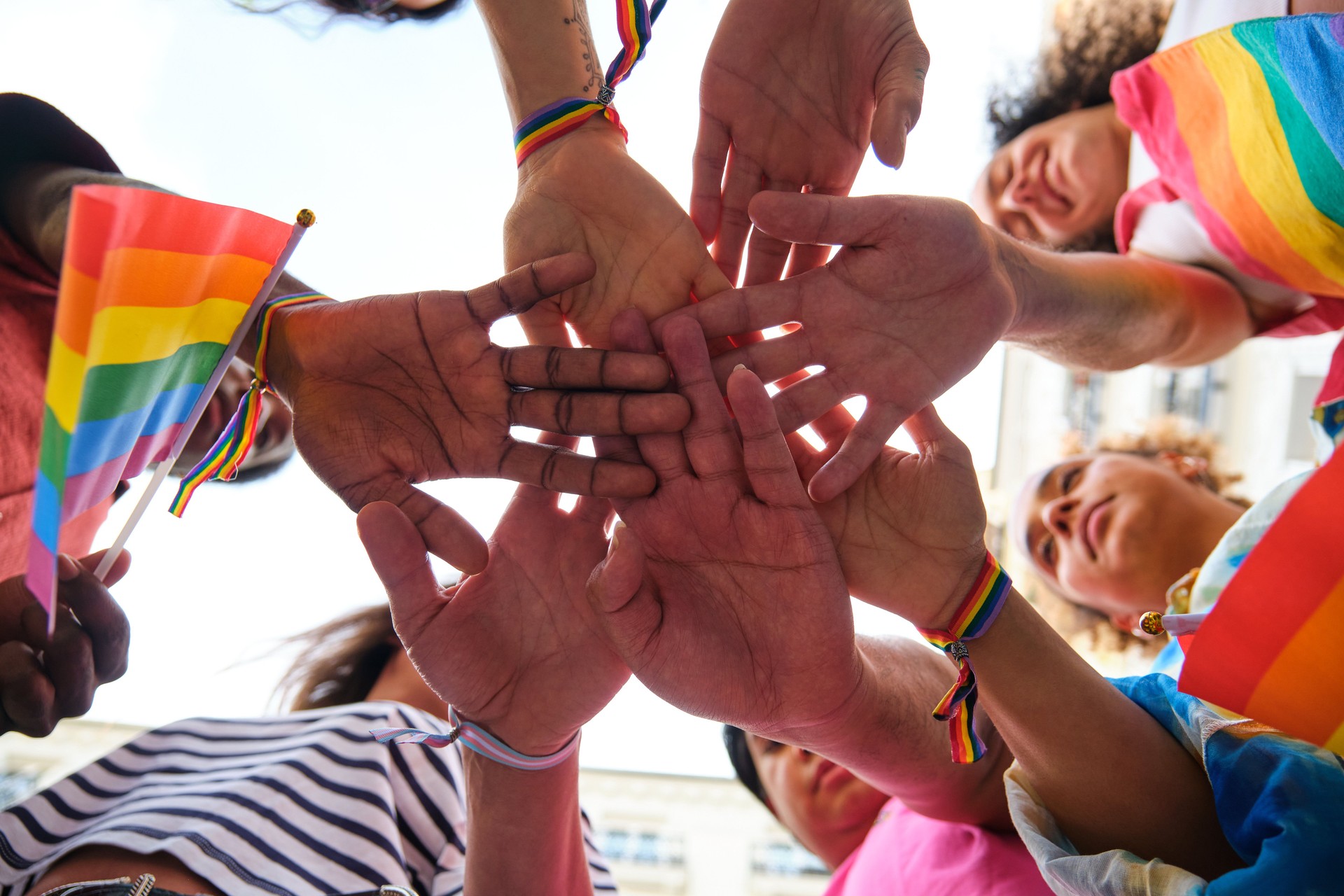 A group of multiracial people with rainbow LGBTQ bracelets stacking hands.